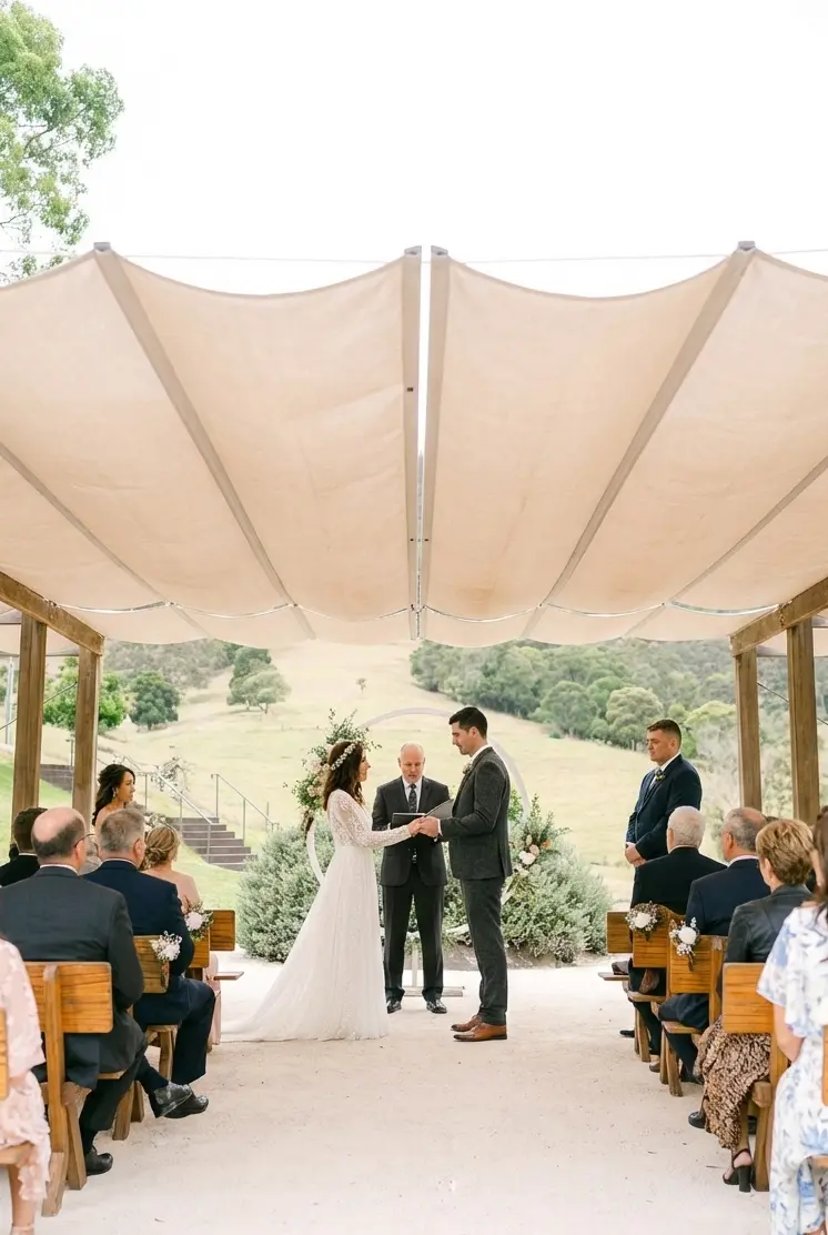 An outdoor wedding ceremony taking place under a white fabric canopy, with guests seated among the trees and views of the Gold Coast hinterland.