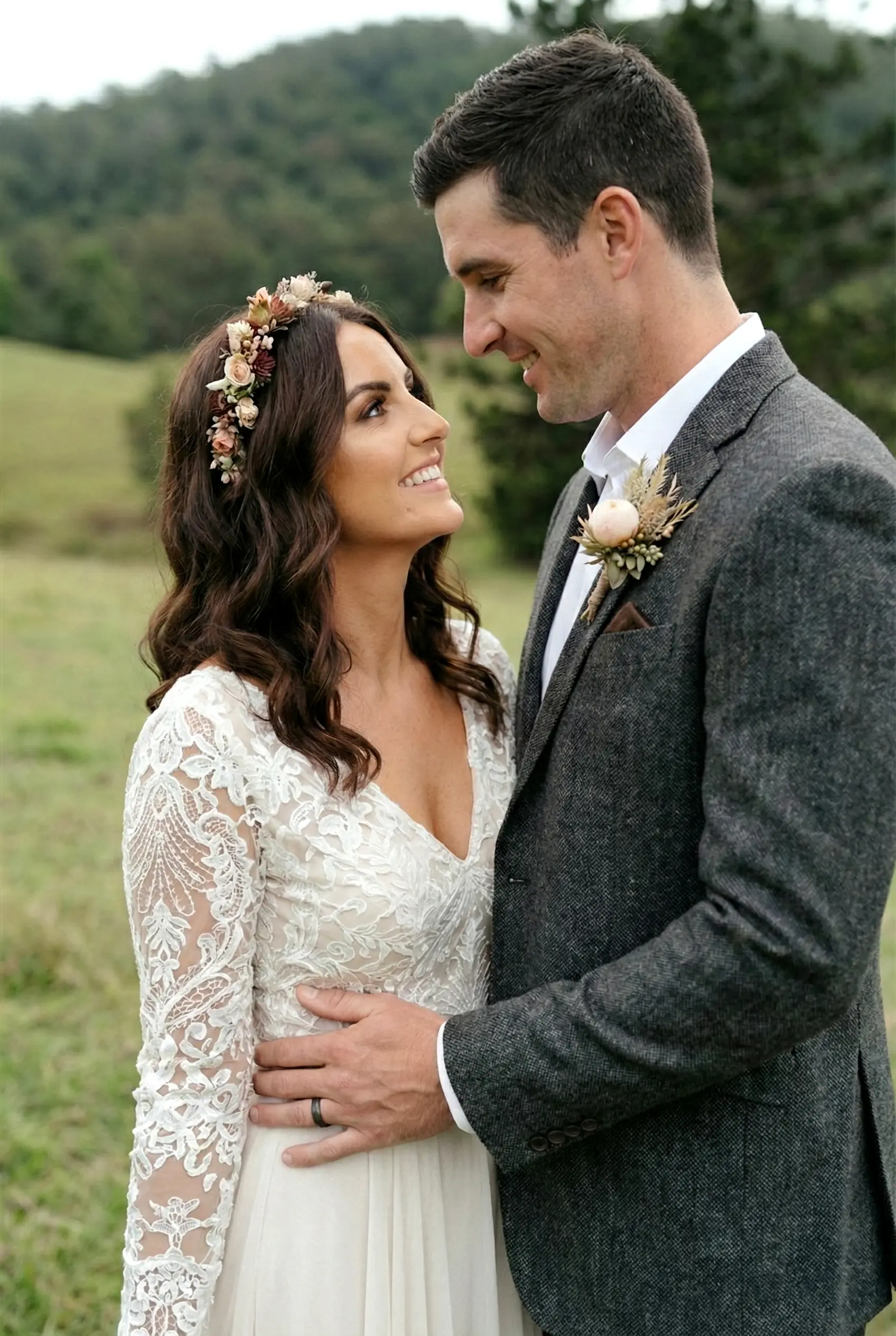 A close-up portrait of a bride in a lace wedding dress and a groom in a charcoal suit sharing an intimate moment in the lush, shaded gardens of Cowbell Creek.