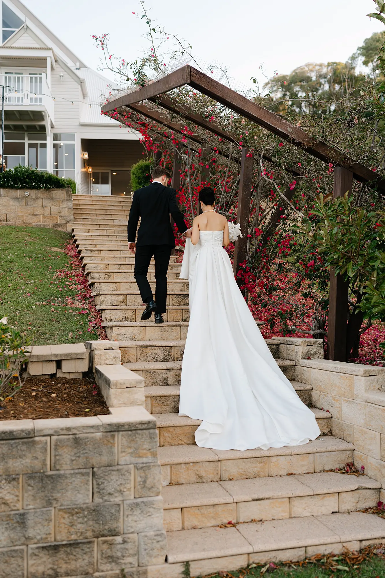 Newlyweds walking up the iconic stone garden stairs at Maleny Manor under a floral pergola.
